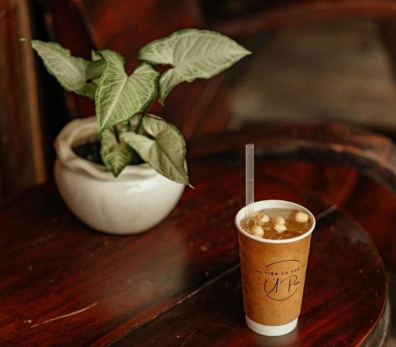 Cốc tr&agrave; sữa tr&ecirc;n b&agrave;n gỗ, b&ecirc;n cạnh l&agrave; chậu c&acirc;y nhỏ trong kh&ocirc;ng gian ấm c&uacute;ng.