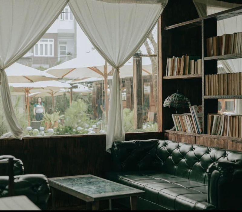 Căn ph&ograve;ng với sofa da, kệ s&aacute;ch v&agrave; cửa sổ lớn nh&igrave;n ra khu vườn c&oacute; &ocirc; che nắng v&agrave; c&acirc;y xanh.