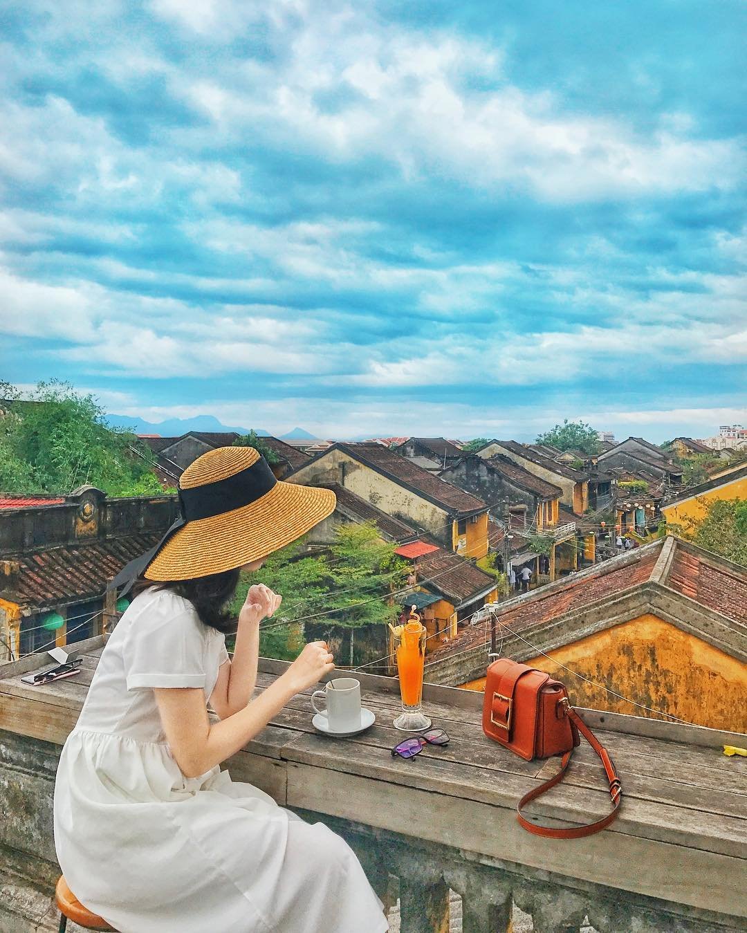Ảnh: @lloollyyyyy Người ngồi trên ban công, nhìn toàn cảnh phố cổ, bên cạnh là tách cà phê và ly nước cam.