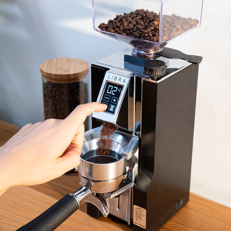 Người điều chỉnh máy xay cà phê với hộc chứa hạt cà phê và màn hình hiển thị kỹ thuật số trên bàn gỗ.