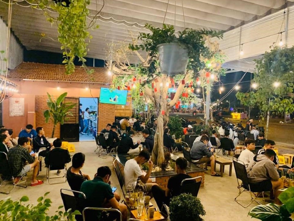 Qu&aacute;n c&agrave; ph&ecirc; ngo&agrave;i trời v&agrave;o ban đ&ecirc;m, nhiều người ngồi uống nước, tr&ograve; chuyện dưới &aacute;nh đ&egrave;n v&agrave; c&acirc;y xanh trang tr&iacute;.