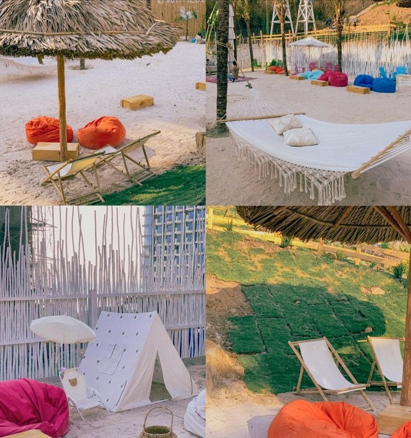 Khu vực nghỉ dưỡng với ghế bãi biển, lều vải, võng và ghế lười trên cát, dưới mái che và cây xanh.