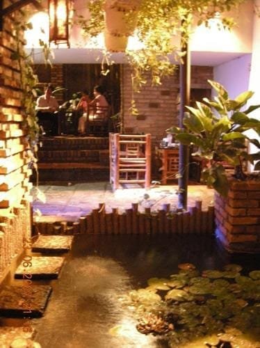 Gợi ý 14 quán cà phê chòi mát mẻ, thư giãn tại TPHCM 13 Quán cà phê với không gian ấm cúng, bàn ghế gỗ, cây xanh và hồ nước nhỏ có hoa súng.