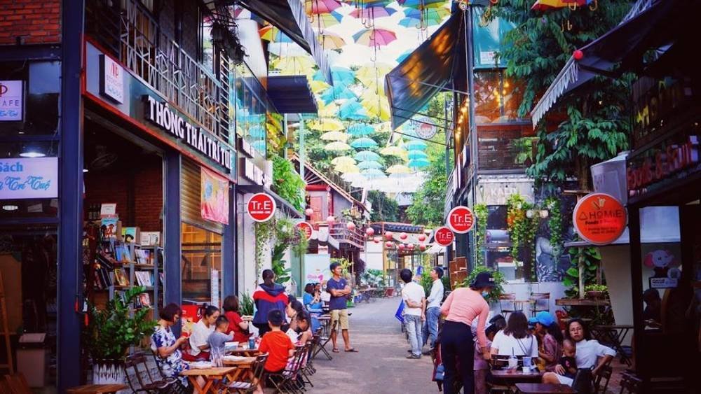 Con đường với nhiều qu&aacute;n c&agrave; ph&ecirc; v&agrave; cửa h&agrave;ng s&aacute;ch, c&oacute; &ocirc; nhiều m&agrave;u treo tr&ecirc;n cao.