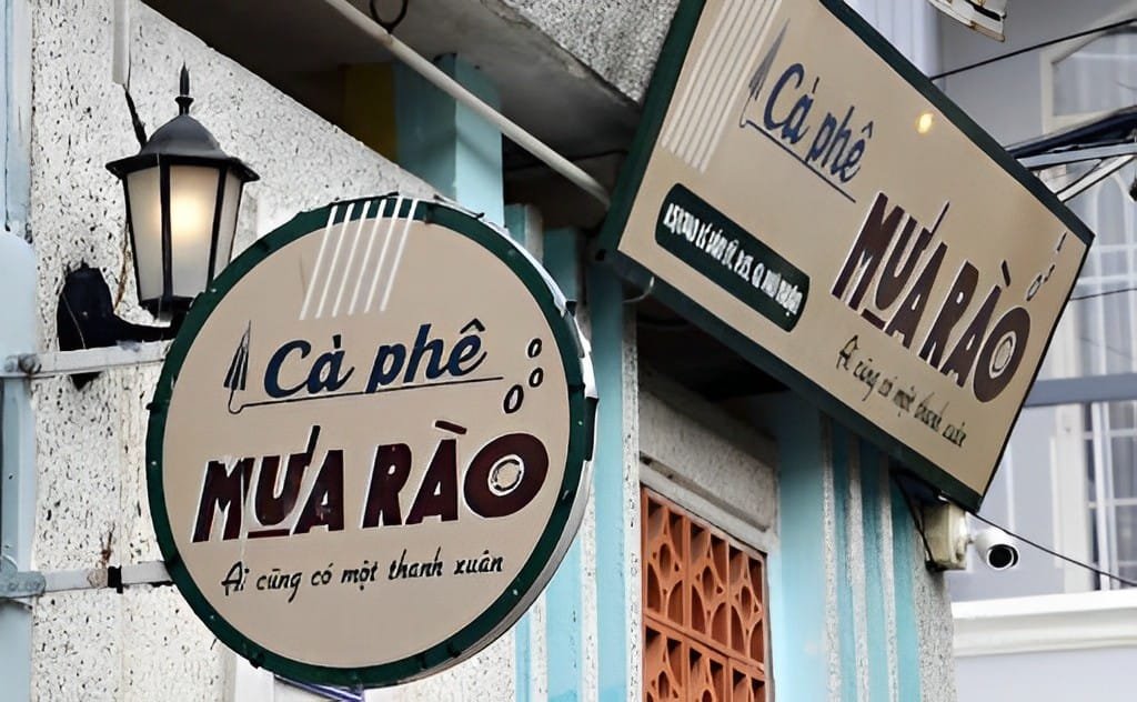 Biển hiệu quán cà phê với thiết kế chữ nổi bật, bên cạnh là đèn treo tường trên nền tường xám.