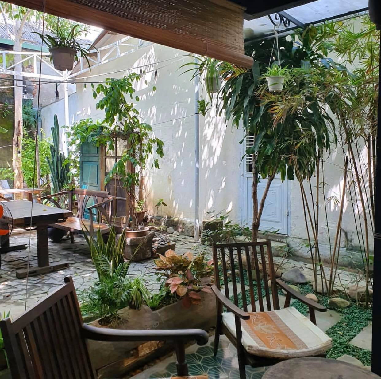 Khu vườn nhỏ với b&agrave;n ghế gỗ, nhiều c&acirc;y xanh v&agrave; &aacute;nh s&aacute;ng tự nhi&ecirc;n chiếu v&agrave;o từ b&ecirc;n ngo&agrave;i.