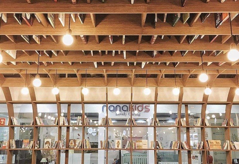 Kh&ocirc;ng gian thư viện với trần gỗ, đ&egrave;n treo, v&agrave; kệ s&aacute;ch được sắp xếp ngăn nắp, tạo cảm gi&aacute;c ấm c&uacute;ng.