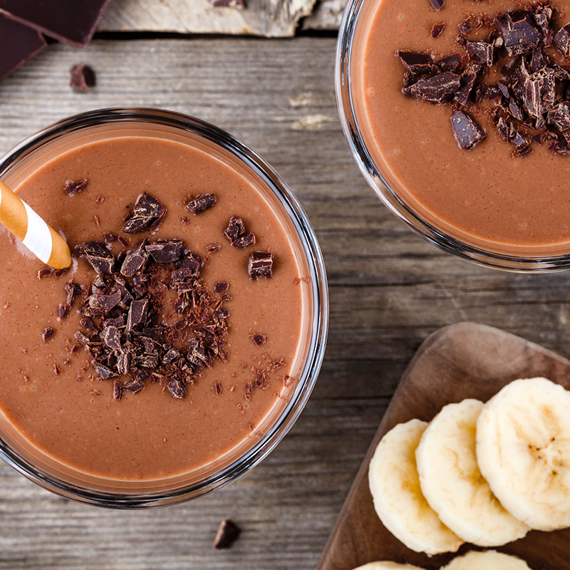 Hai ly sinh tố sô cô la trang trí vụn sô cô la, cạnh đĩa chuối lát trên nền gỗ.