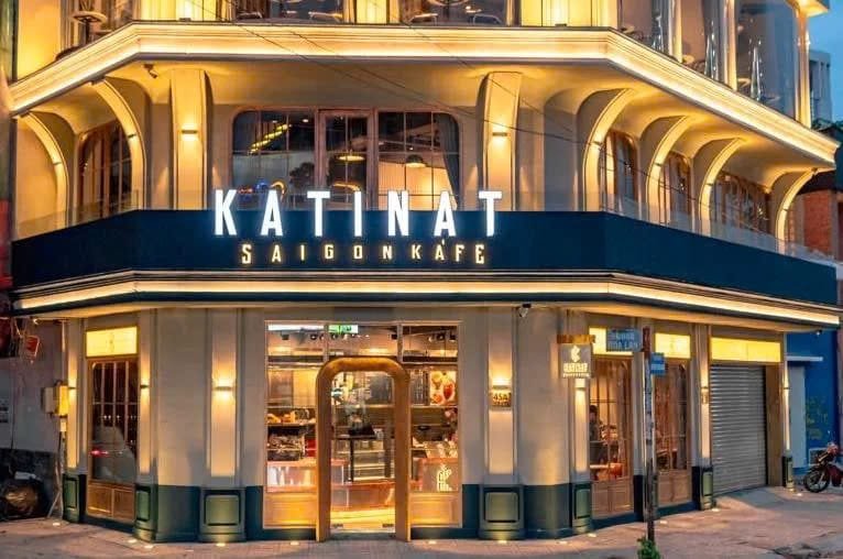 Mặt tiền quán cà phê với kiến trúc hiện đại, cửa kính lớn và biển hiệu sáng đèn vào buổi tối.